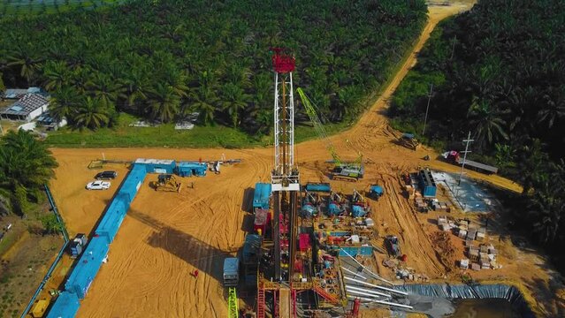 Cinematic Onshore Drilling and Workover Rig structure and Rig equipment for oil exploration and exploitation in the middle of jungle surrounded by palm oil trees during sunset time.