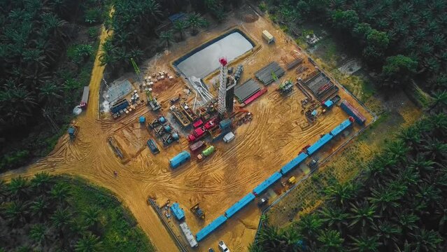 Cinematic Onshore Drilling and Workover Rig structure and Rig equipment for oil exploration and exploitation in the middle of jungle surrounded by palm oil trees during sunset time.