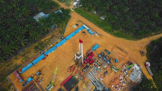 Cinematic Onshore Drilling and Workover Rig structure and Rig equipment for oil exploration and exploitation in the middle of jungle surrounded by palm oil trees during sunset time.