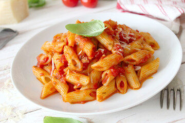 Penne pasta with tomato sauce, parmesan cheese and pasil on wooden table. Top view.