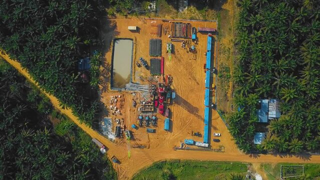 Cinematic Onshore Drilling and Workover Rig structure and Rig equipment for oil exploration and exploitation in the middle of jungle surrounded by palm oil trees during sunset time.