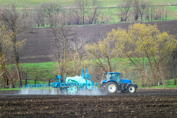Tractor spraying insecticide on cultivated land field. Agricultural agronomy machinery in work on a spring day. Rural view	