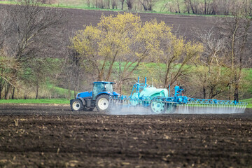 Tractor spraying insecticide on cultivated land field. Agricultural agronomy equipment in work in spring farmland. Rural landscape	