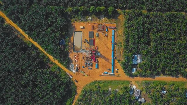 Cinematic Onshore Drilling and Workover Rig structure and Rig equipment for oil exploration and exploitation in the middle of jungle surrounded by palm oil trees during sunset time.