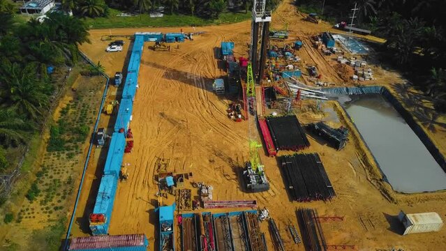 Cinematic Onshore Drilling and Workover Rig structure and Rig equipment for oil exploration and exploitation in the middle of jungle surrounded by palm oil trees during sunset time.