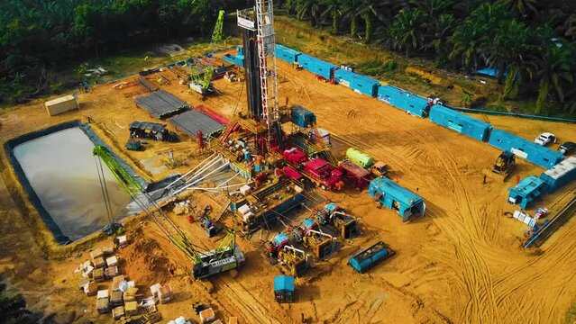 Cinematic Onshore Drilling and Workover Rig structure and Rig equipment for oil exploration and exploitation in the middle of jungle surrounded by palm oil trees during sunset time.