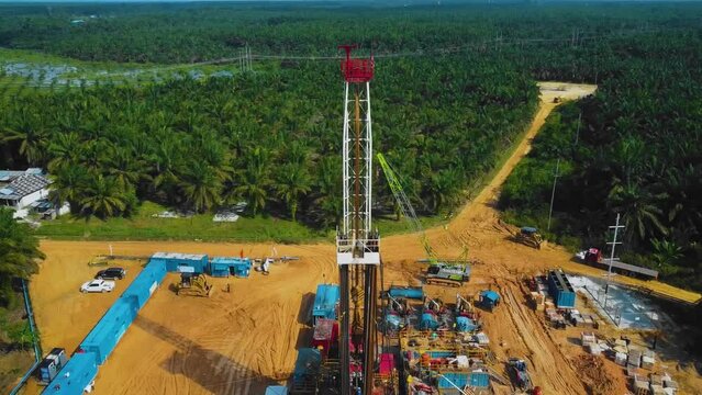 Cinematic Onshore Drilling and Workover Rig structure and Rig equipment for oil exploration and exploitation in the middle of jungle surrounded by palm oil trees during sunset time.