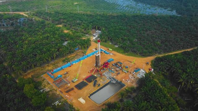 Cinematic Onshore Drilling and Workover Rig structure and Rig equipment for oil exploration and exploitation in the middle of jungle surrounded by palm oil trees during sunset time.
