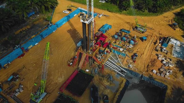 Cinematic Onshore Drilling and Workover Rig structure and Rig equipment for oil exploration and exploitation in the middle of jungle surrounded by palm oil trees during sunset time.