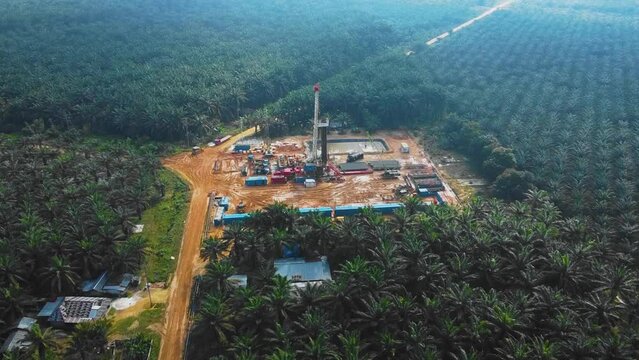 Cinematic Onshore Drilling and Workover Rig structure and Rig equipment for oil exploration and exploitation in the middle of jungle surrounded by palm oil trees during sunset time.