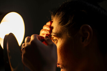 a natural girl at home plucks her eyebrows and paints her eyes, the front and background are blurred with a bokeh effect