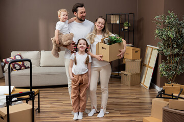 Fototapeta na wymiar Couple in love moves into a new apartment with their children, they bring cardboard boxes with packed things into the living room, a woman sets up decorations, they decorate their first home together.