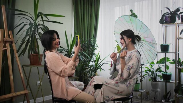 A young woman takes a picture of a girl in the form of a geisha on the phone. Creating an image for a photo shoot