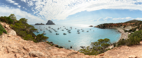 Maxi panoramic shot of a horseshoe-shaped bay Cola d'Hort, pre-sunset sun whitened water with its rays, Ibiza, Balearic Islands, Spain