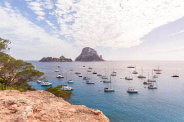 Anchored catamarans and sailing yachts in bay Cola d'Hort against backdrop of two lovely rocky islands Es Vedra and Es Vedranell. Ibiza, Balearic Islands, Spain