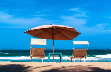 A portrait of a pair of beach chairs with umbrella in a seashore. Vacation concept, waterfront relaxation image. 