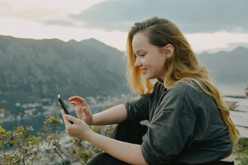 Woman on top of a mountain in Montenegro, Kotor. The girl looks at the smartphone, writes something, prints.