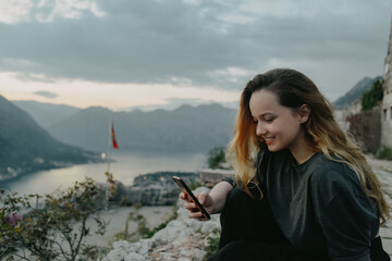 Woman on top of a mountain in Montenegro, Kotor. The girl looks at the smartphone, writes something, prints.