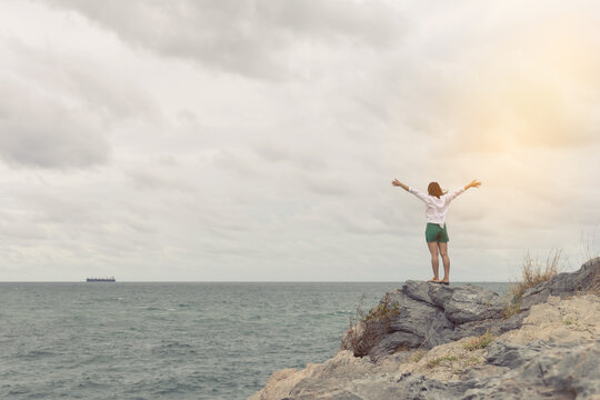 Woman Standing With Arms Spread Out On The Rocks By The Sea.