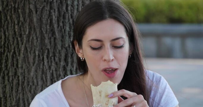Beautiful young woman eating tasty shawarma outdoors