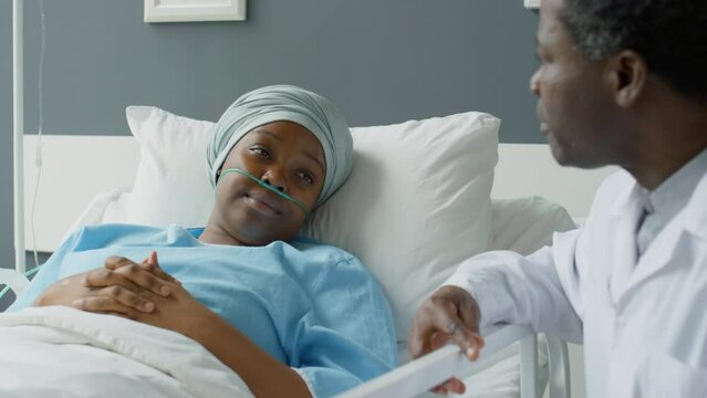 African American woman with nasal cannula and headwrap lying on hospital bed and talking with doctor during his visit