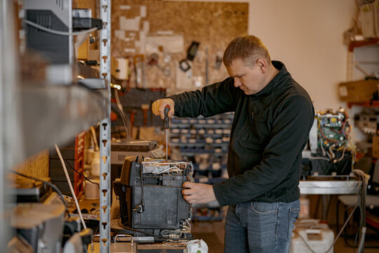 Repairman with screwdriver fixing coffee machine at table indoors