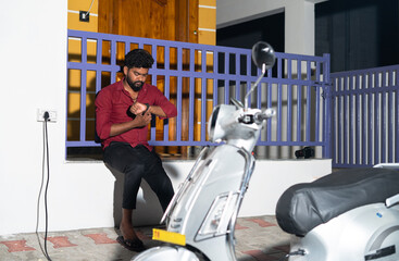 Man waiting for ev or electric scooter battery to charge near home at night - concept of delayed...