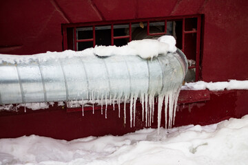 Galvanized heating pipe covered with icicles in winter, heating of non-residential premises