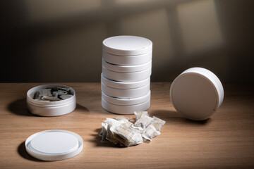 Studio shot of white swedish smokeless tobacco cans and portion snus pouches on a wooden table.