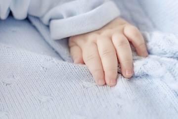 The baby arm lie on a woolen warm blue blanket top view. Care for baby's delicate skin....