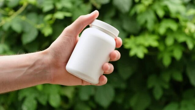 A white plastic bottle with lid in man's hand shaking. Close up, copy space, place for label or branding.