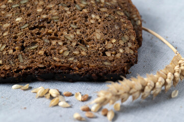 Slices of dark bread with seeds on natural linen background with dried wheats.