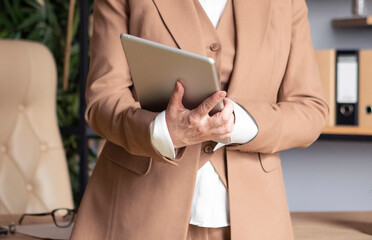 Fototapeta na wymiar business woman in a beige suit working at the office, typing on tablet