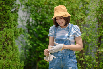 An Asian woman gardener is taking off her gloves after finishing her work.