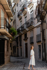 Fototapeta na wymiar redhead woman in dress standing near houses on european street in valencia.