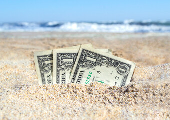 Three paper cash one dollar bills half buried in the sand on the seashore close-up. Concept money,...