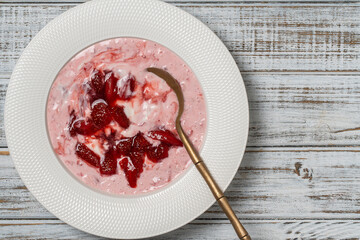 White plate with red strawberries and natural yogurt on a wooden table, top view