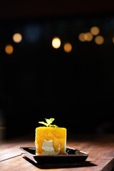 let's tea time, yellow mnago cake topping with mint leaf in black ceramic plate on wood table with bokeh background