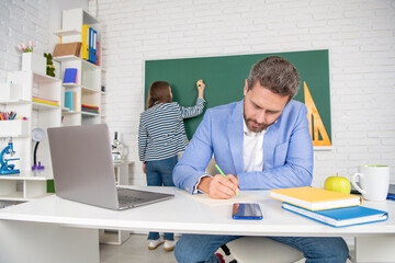 school teacher in classroom with selective focus of kid at blackboard