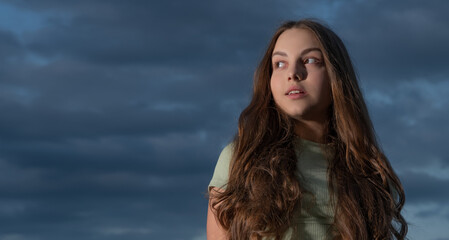 teen girl with long curly hair on sky background with copy space