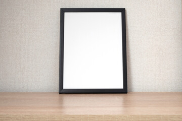 Black photo frame with blank white space on wooden shelf, desk. Mockup, template space for text