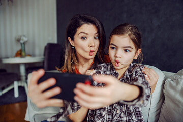 Mother and daughter making silly faces and taking a selfie. - obrazy, fototapety, plakaty