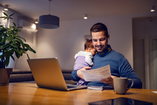 A happy entrepreneur looking at documents while babysits his daughter and working remotely from home.