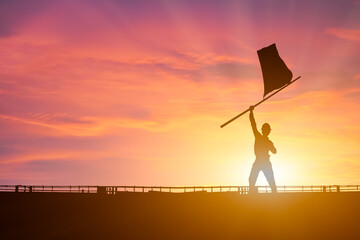 Silhouette of businessman holding a flag on top mountain, sky and sun light background.
