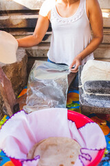 Mujer mexicana torteando maza de maíz en un metate y una estufa de leña para hacer tortillas...