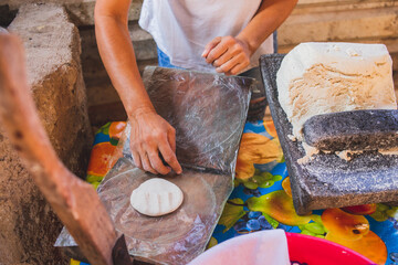 Mujer mexicana torteando maza de maíz en un metate y una estufa de leña para hacer tortillas caseras	
 - obrazy, fototapety, plakaty