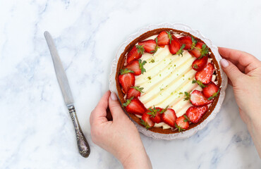 In women's hands delicious homemade tart with strawberries, cream cheese or whipped cream, jelly and pistachios. Berry cheesecake. Dessert. Pie. Cake. Marble background. Top view, copy space