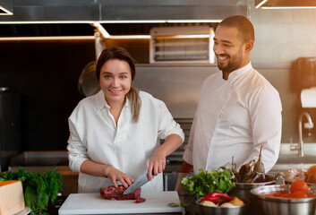 Handsome young African chef is cooking together with his Caucasian girlfriend in the kitchen using red wine as an ingredient.