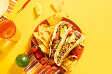 Traditional Mexican food corn tacos with meat, vegetables, avocado, beans, corn, salsa and nachos. Served with various sauces and drinks on yellow background. Top view. Big family gatherings.