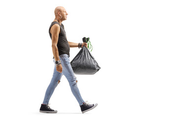 Full length profile shot of a bald man in ripped jeans carrying a plastic waste bag